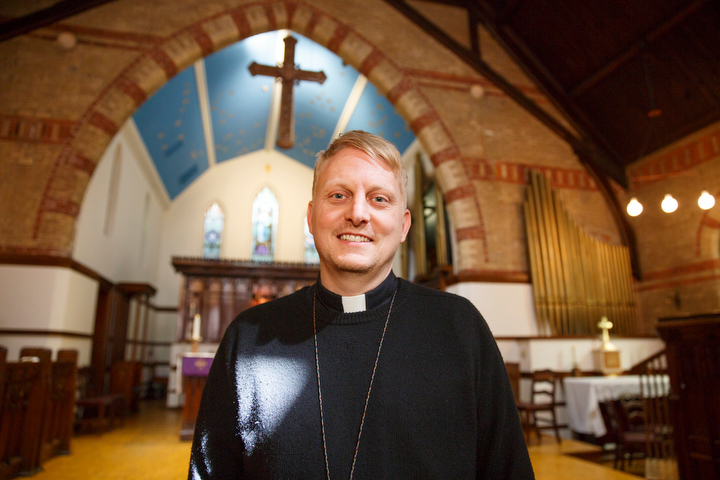 A man in robes and a clerical collar with the interior of the church in the background